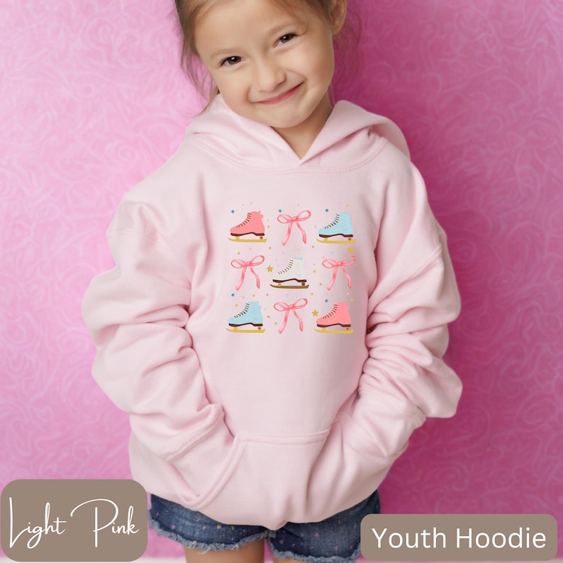 May include: Light pink youth hoodie featuring a pattern of ice skates and bows in pink, blue, and white. The hoodie has a kangaroo pocket and a hood. The text "Youth Hoodie" is at the bottom right.