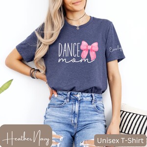 Może przedstawiać: Uniseksowa koszulka w kolorze granatowym melanżowym z napisem "Dance Mom" i r&oacute;żową akwarelową kokardką. Koszulka ma spersonalizowane imię "Evelyn" po prawej stronie.