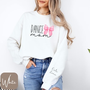 Może przedstawiać: Biała bluza z napisem "DANCE mom" i r&oacute;żową kokardką. Na rękawie znajduje się napis "Kate Luna".
