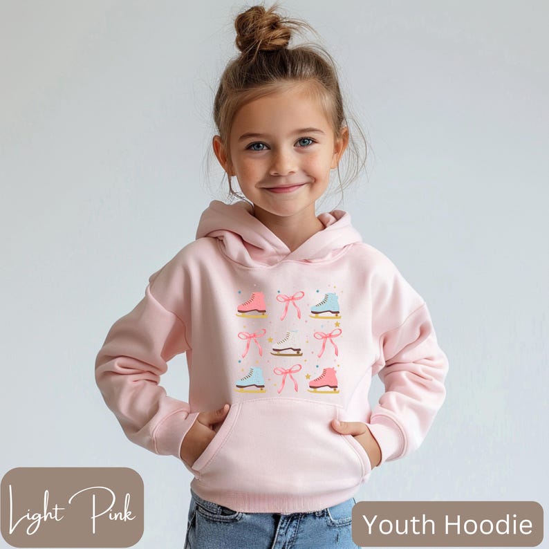 May include: Light pink youth hoodie featuring a pattern of ice skates and bows. The design includes pink, blue, and white skates with matching bows. The hoodie has a front pocket and a hood. The text "Light Pink" and "Youth Hoodie" are visible.