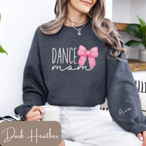 Może przedstawiać: Szara bluza w kolorze ciemnego melanżu z napisem "Dance Mom" i r&oacute;żową kokardką. Bluza ma wyszyte imię "Ava" na rękawie.