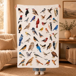 Peut inclure: Une couverture en polaire blanche ornée d'un imprimé détaillé représentant diverses espèces d'oiseaux nord-américains, notamment des cardinaux, des geais bleus, des hiboux, des pics et des colibris, disposés sur toute la surface du tissu.