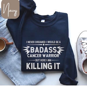 May include: Navy blue sweatshirt with a white graphic that reads "I never dreamed I would be a badass cancer warrior but here I am killing it".