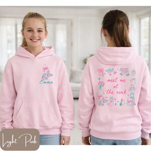 May include: Light pink hoodie with a front pocket and a hood. The front features a teal and pink ice skate design with the name "Emma". The back has a "meet me at the rink" design with ice skates, flowers, and other graphics.