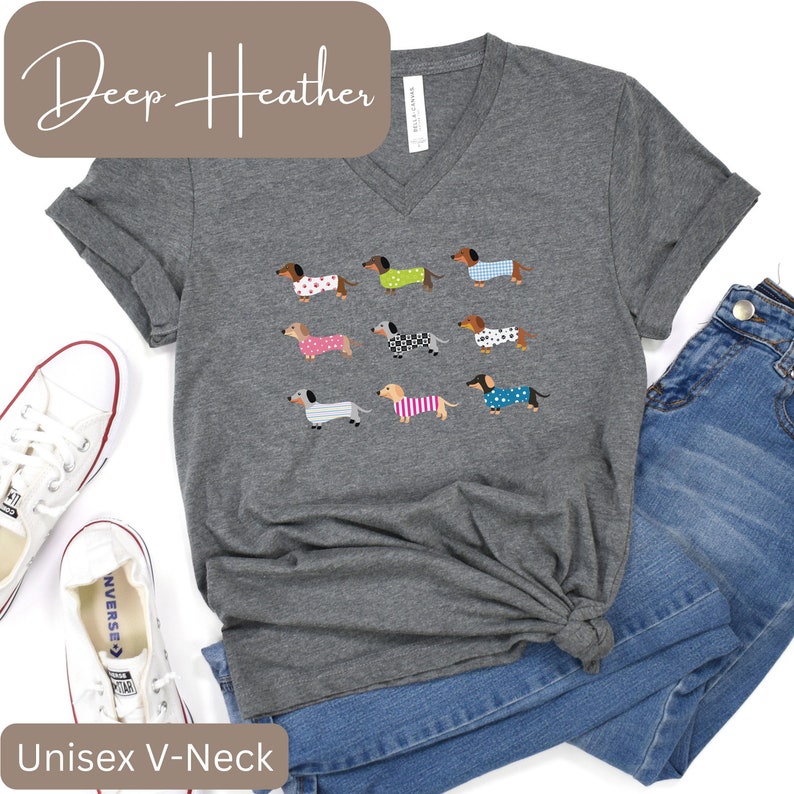 May include: Deep heather grey unisex V-neck t-shirt with a pattern of dachshunds in different outfits. The shirt is styled with blue jeans and white trainers. The text "Deep Heather" and "Unisex V-Neck" are displayed.