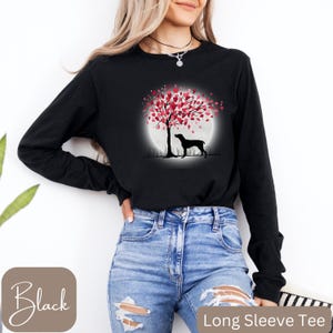 May include: Black long-sleeved T-shirt featuring a graphic of a dog standing in front of a tree with pink heart-shaped leaves. The tree is in front of a full moon.