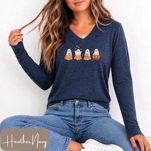 May include: A heather navy long-sleeve V-neck shirt featuring a graphic of four white ghosts with orange-tinted bottoms. The ghosts are depicted holding various items, including a pumpkin, and are surrounded by small orange autumn leaves.