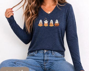 May include: A heather navy long-sleeve V-neck shirt featuring a graphic of four white ghosts with orange-tinted bottoms. The ghosts are depicted holding various items, including a pumpkin, and are surrounded by small orange autumn leaves.