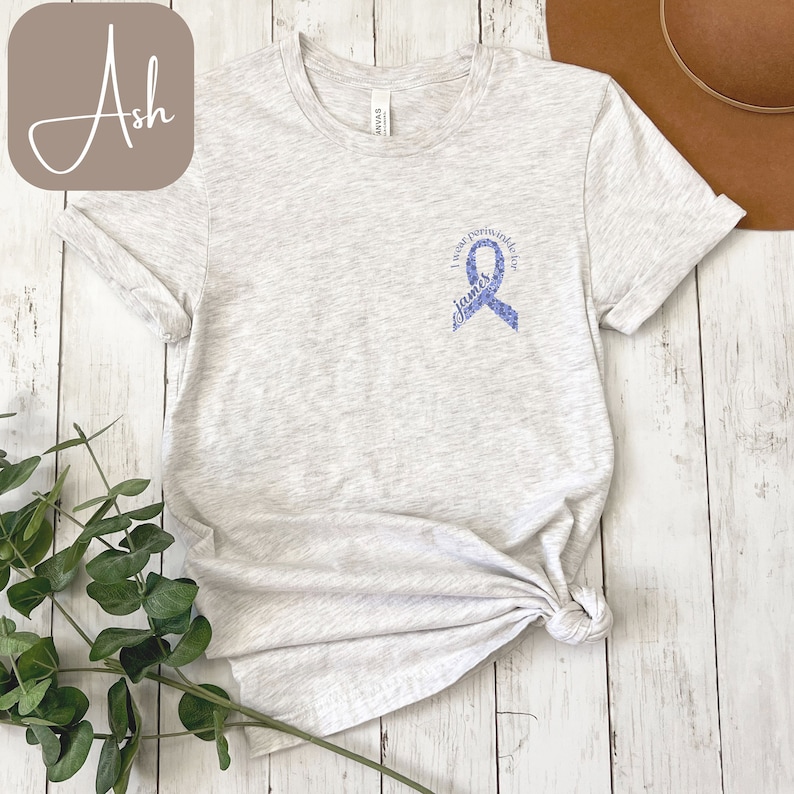 May include: A light gray t-shirt with a purple ribbon and the text "I wear purple for James".