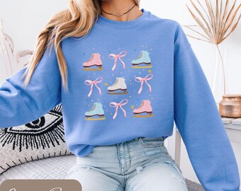 以下が含まれることがあります： ピンク、白、青のスケート靴とピンクのリボンが繰り返されるパターンが特徴の、カロライナブルーのユニセックススウェットシャツ。「Carolina Blue」と「Unisex Sweatshirt」の文字も表示されています。
