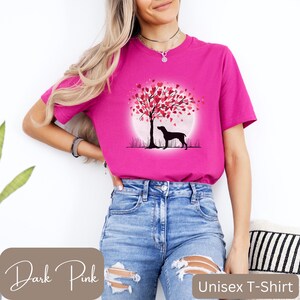 May include: A dark pink unisex t-shirt featuring a graphic of a black dog standing beneath a tree with pink heart-shaped leaves. The tree is positioned in front of a full moon.