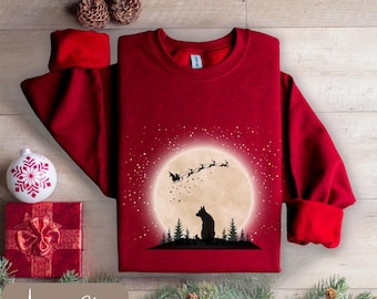 Op de afbeelding: Een bordeauxrode sweatshirt met een afbeelding van een hond die kijkt naar de slee van de kerstman voor een volle maan. De tekst "Antique Cherry" staat onderaan. Kerstkleding.