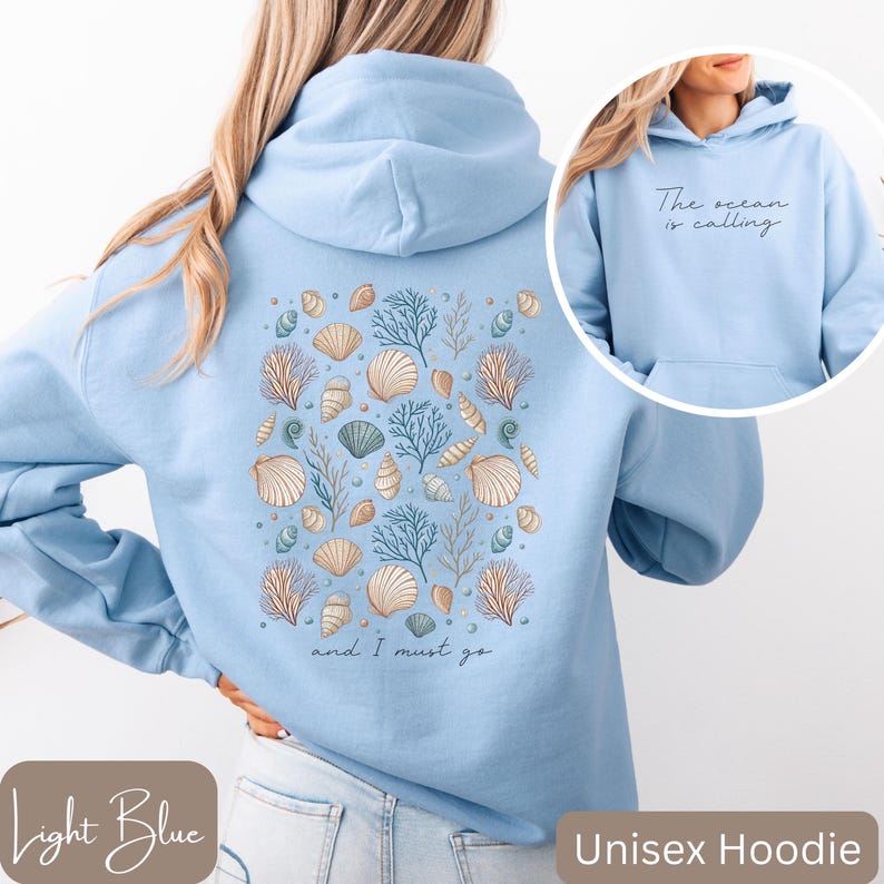 K&ouml;nnte beinhalten: Hellblauer Unisex-Hoodie mit einem Muschel- und Korallendesign auf der R&uuml;ckseite. Der Text "The ocean is calling and I must go" ist auf der R&uuml;ckseite des Hoodies aufgedruckt.