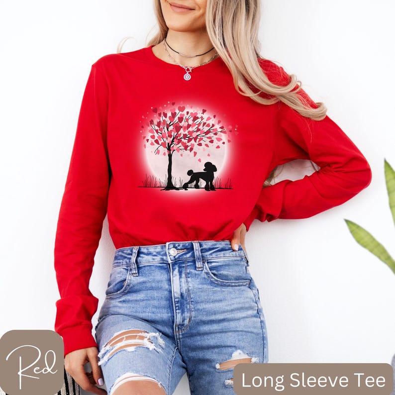 Op de afbeelding: Rood longsleeve t-shirt met een afbeelding van een poedel die onder een boom staat met roze harten als bladeren. De boom staat voor een volle maan.