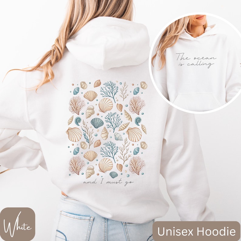 K&ouml;nnte beinhalten: Wei&szlig;er Unisex-Hoodie mit einem Muschel- und Korallendesign auf der R&uuml;ckseite. Der Text "and I must go" ist unter dem Design gedruckt. Die Vorderseite des Hoodies hat den Text "The ocean is calling" auf der Vorderseite.