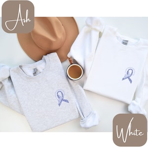 May include: Two sweatshirts with a purple ribbon design. The text on the ribbon says "In my heart forever for my dad". One sweatshirt is ash grey and the other is white.