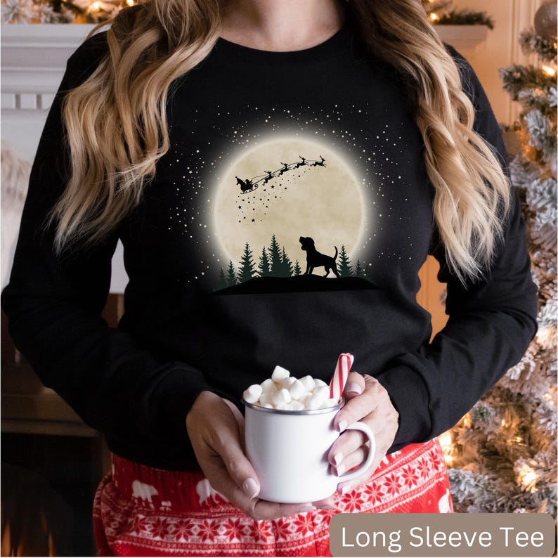 May include: Black long sleeve tee with a graphic of a dog silhouetted against a full moon, with Santa and his reindeer flying above. The text "Long Sleeve Tee" is at the bottom of the image.