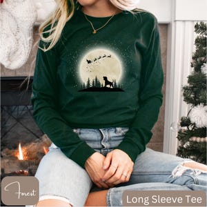May include: A dark green long-sleeve tee with a graphic of a dog silhouette under a full moon with Santa's sleigh and reindeer. The shirt has the text "Long Sleeve Tee" at the bottom.