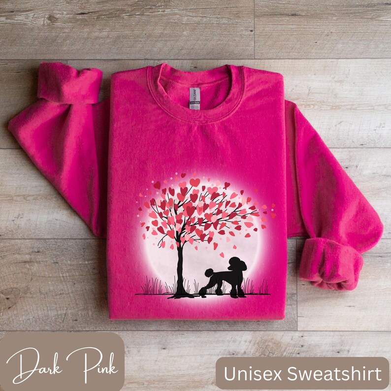 Op de afbeelding: Een donkerroze unisex sweatshirt met een afbeelding van een poedel die onder een boom staat met harten als bladeren. De boom staat voor een volle maan.