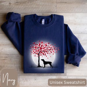 May include: Navy blue unisex sweatshirt featuring a graphic of a dog standing under a tree with pink hearts in the shape of a full moon. The text "Unisex Sweatshirt" is printed on the bottom right corner of the image and the text "Navy" is printed on the bottom left corner of the image.