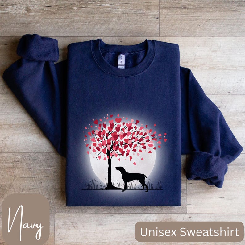 May include: Navy blue unisex sweatshirt featuring a graphic of a dog standing under a tree with pink hearts in the shape of a full moon. The text "Unisex Sweatshirt" is printed on the bottom right corner of the image and the text "Navy" is printed on the bottom left corner of the image.