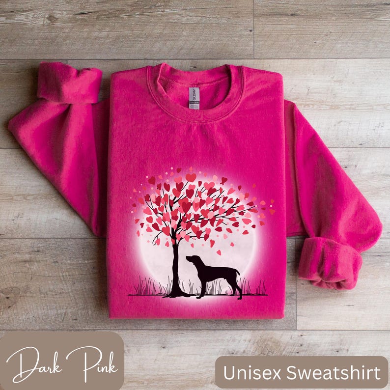 May include: A dark pink unisex sweatshirt featuring a graphic of a dog standing beneath a tree with hearts for leaves. The tree is encircled by a white circle with a light pink gradient.