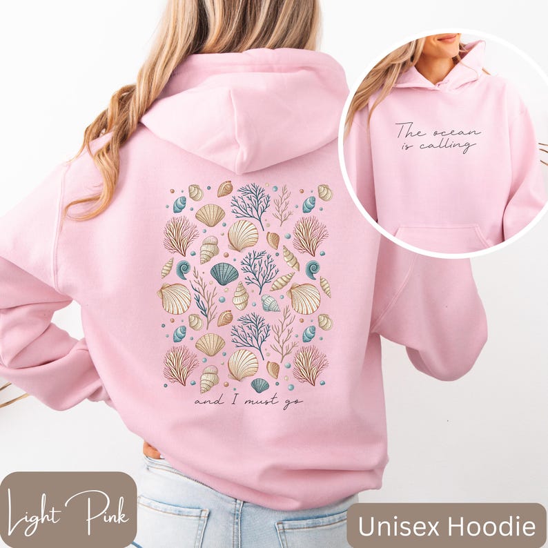 K&ouml;nnte beinhalten: Hellrosa unisex Hoodie mit einem Muschel- und Korallendesign auf der R&uuml;ckseite. Der Text "The ocean is calling and I must go" ist auf der R&uuml;ckseite des Hoodies aufgedruckt.