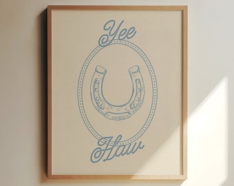 May include: A framed print with a blue horseshoe design in a circle with the text "Yee Haw" underneath. The background is a light beige color.