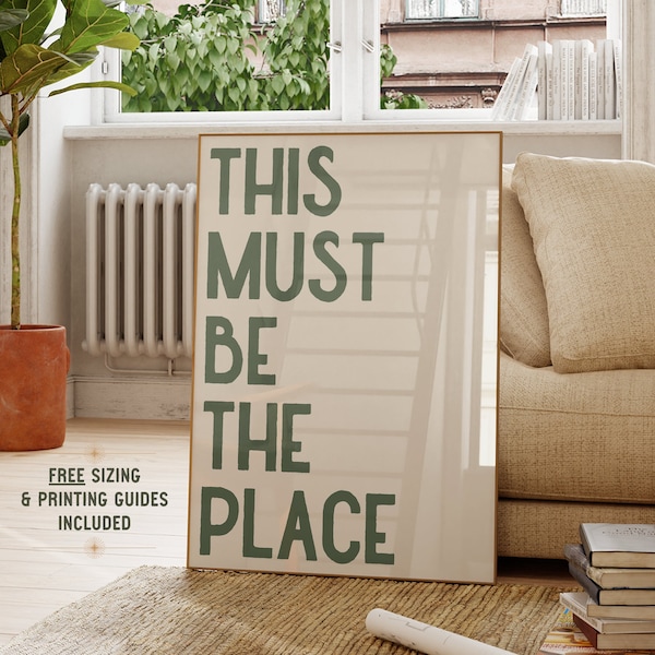 以下が含まれることがあります： ベージュの背景に緑色の文字で「THIS MUST BE THE PLACE」と書かれた額装されたプリント。プリントはリビングルームの壁に飾られています。