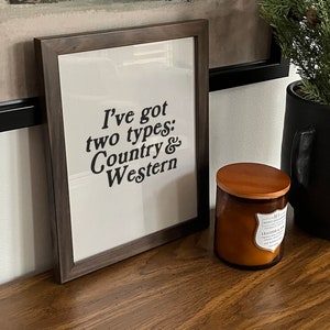 May include: A framed print with the text "I've got two types: Country & Western" in black lettering on a white background. The frame is dark brown wood.