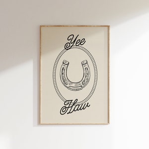 Pu&ograve; includere: Un'illustrazione in bianco e nero di un ferro di cavallo in un cerchio con le parole "Yee Haw" scritte in un font corsivo.