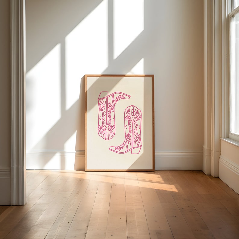 May include: A framed print of a pair of pink cowboy boots with intricate designs on a white background.
