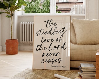 May include: A beige framed print with black calligraphy that reads "The steadfast love of the Lord never ceases, Lamentations 3:22".