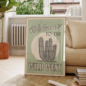 以下が含まれることがあります： 「Welcome to the Wild West」というテキストと、黒と白の線画で描かれたサボテンが描かれた緑と白のポスターです。