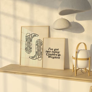 May include: Two framed prints on a wooden shelf. The print on the left shows a line drawing of two cowboy boots. The print on the right has the text "I've got two types: Country & Western".