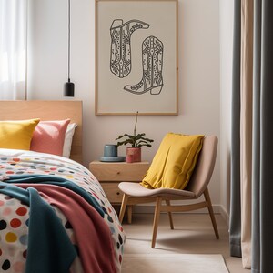 May include: A bedroom with a bed, a chair, a nightstand, and a framed print of two cowboy boots. The bed has a white and colorful polka dot duvet cover, a pink blanket, and a blue blanket. The chair is wooden with a yellow pillow. The nightstand is wooden with a small plant on top. The print is on a beige background with black outlines.