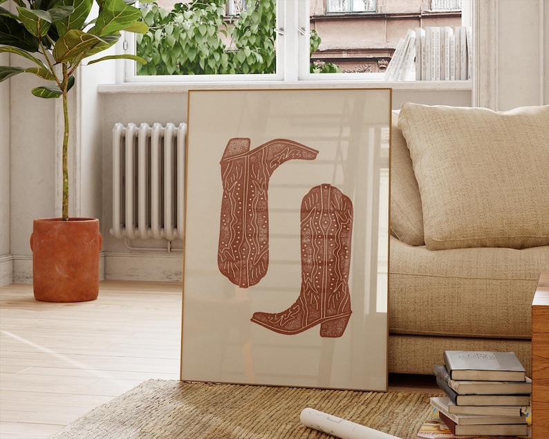 Pu&ograve; includere: Una stampa incorniciata di due stivali da cowboy marroni con motivi intricati. Gli stivali sono su uno sfondo crema.
