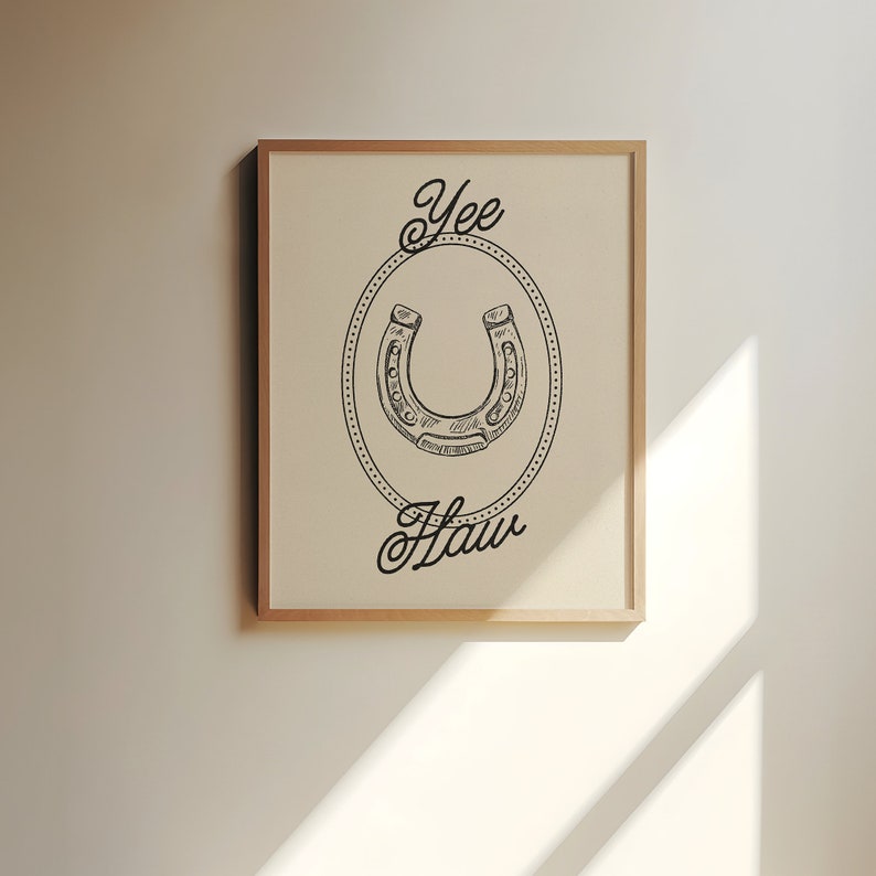 Pu&ograve; includere: Una stampa incorniciata con un'illustrazione in bianco e nero di un ferro di cavallo in un cerchio con il testo "Yee Haw" sotto.