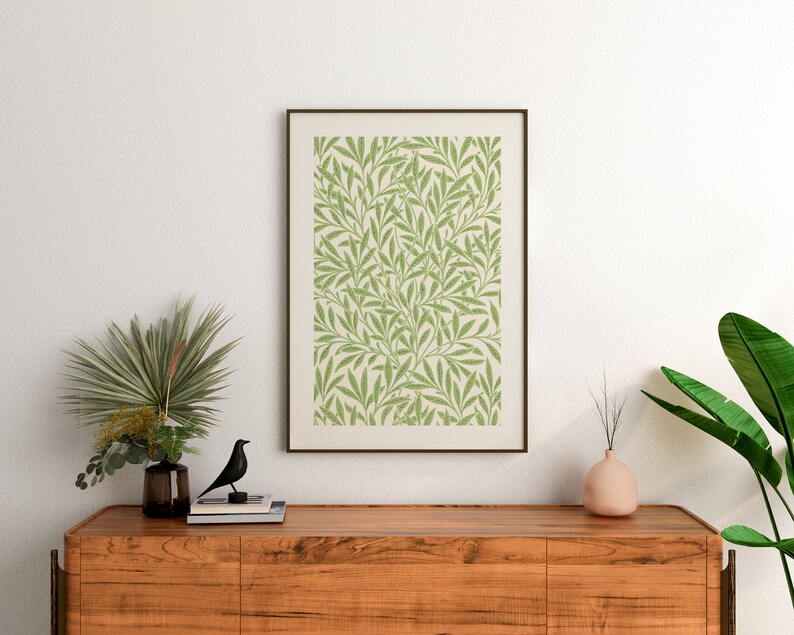 May include: A framed print featuring a green and white floral design hangs above a wooden dresser. The dresser has a vase with a green plant and a black bird figurine on top.