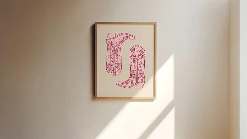 May include: A framed print of two pink cowboy boots with intricate designs. The boots are outlined in a darker pink and are set against a white background.