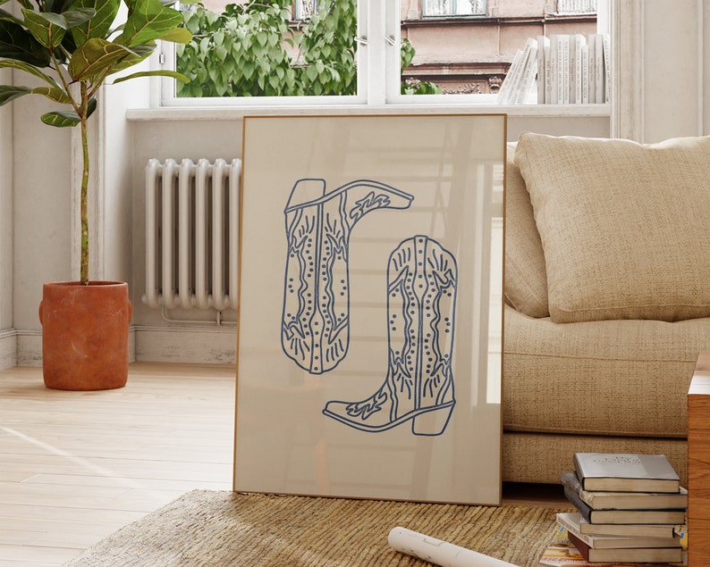 Op de afbeelding: Een ingelijst afdruk van een paar blauwe cowboylaarzen met ingewikkelde ontwerpen op een beige achtergrond.