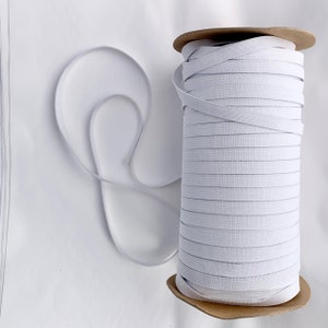 May include: A spool of white elastic cord, wound tightly on a cardboard core. The elastic is smooth and appears to be about 1/4 inch wide.