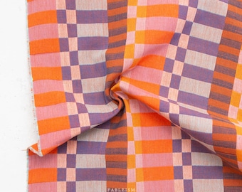 May include: A woven fabric featuring a repeating plaid pattern in vibrant shades of orange, light pink, and deep purple. The textile displays a structured grid design with visible horizontal and vertical threads. The word FABLEISM is printed in white.