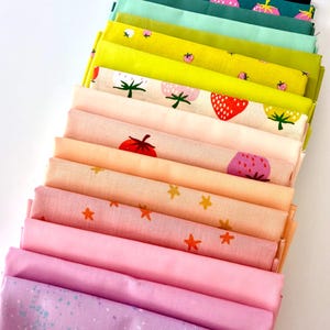 May include: A stack of colorful fabric swatches in shades of pink, yellow, and green. Some fabrics feature strawberry and star patterns. The top swatch is dark green with a strawberry print. The fabrics are neatly arranged, showcasing a variety of textures and designs.