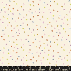 May include: Off-white fabric with a scattered pattern of colorful stars in shades of orange, yellow, green, blue, purple, and pink. The stars are randomly arranged across the fabric's surface. The bottom of the fabric has the text "RUBY STAR SOCIETY".