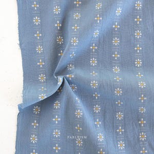 May include: Close-up of a blue fabric with a repeating floral pattern in white and yellow. The fabric has a slightly textured appearance and the word "FABLEISM" is printed in white at the bottom right.