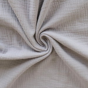 May include: A close-up of a soft, light gray fabric with a crinkled texture. The fabric is folded and draped, creating a swirling pattern.