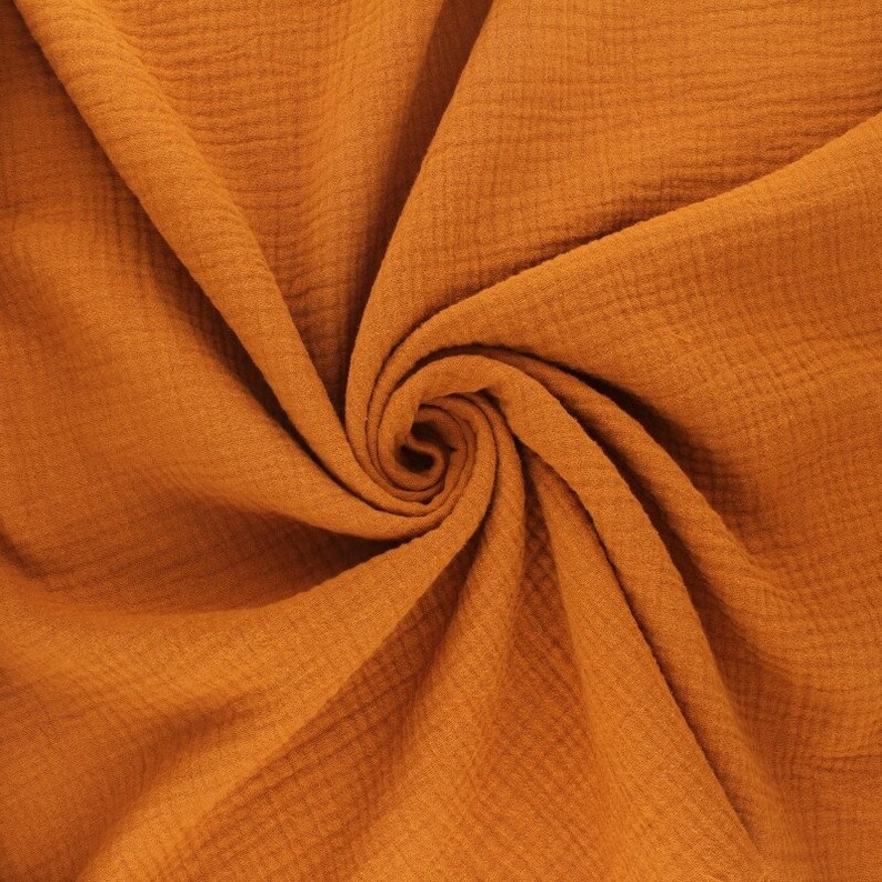 May include: A close-up of a soft, textured fabric in a warm, burnt orange color. The fabric is folded and draped, showcasing its crinkled texture.