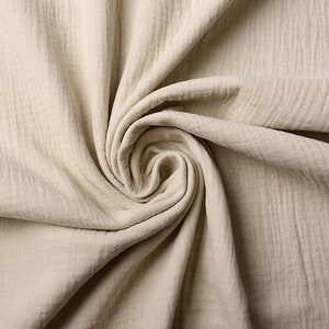 May include: A close-up of a beige fabric with a textured surface. The fabric is folded and twisted, creating a swirling pattern.