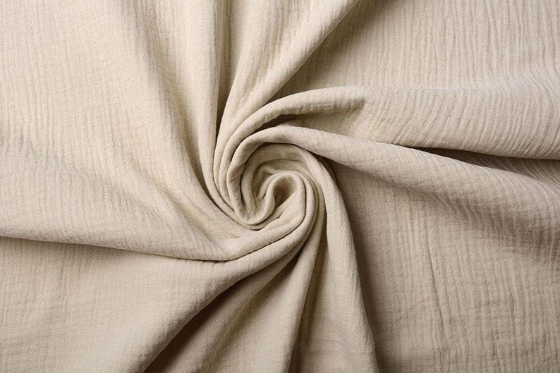 May include: A close-up of a beige fabric with a textured surface. The fabric is folded and twisted, creating a swirling pattern.